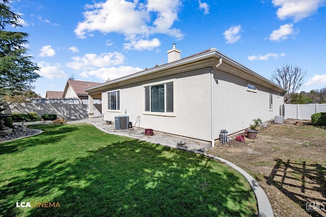 rear view of house featuring fence, central AC, stucco siding, a lawn, and a chimney