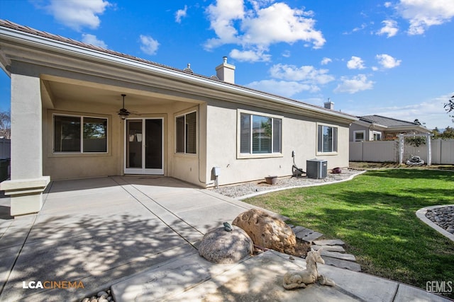 rear view of property with stucco siding, a lawn, a ceiling fan, a patio, and fence