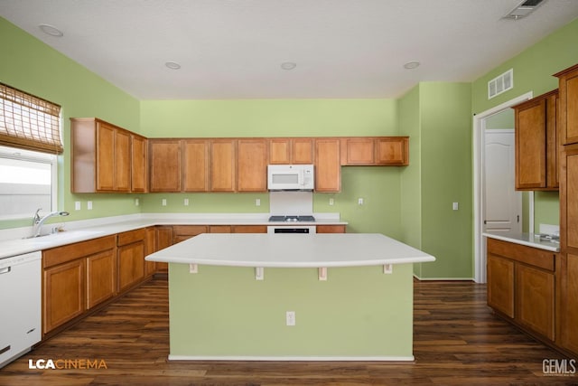 kitchen featuring visible vents, a kitchen island, dark wood finished floors, white appliances, and a sink