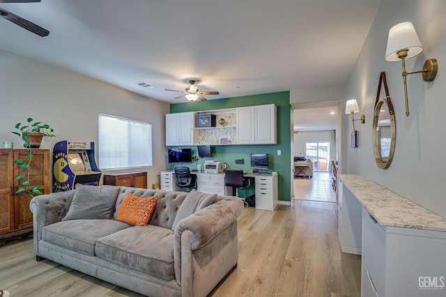 living room featuring light wood-type flooring, built in desk, visible vents, and a ceiling fan