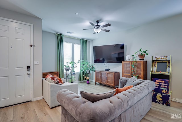 living room featuring visible vents, baseboards, a ceiling fan, and light wood finished floors