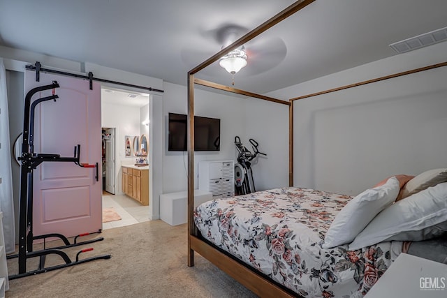 bedroom featuring visible vents, light colored carpet, a barn door, ensuite bath, and a ceiling fan