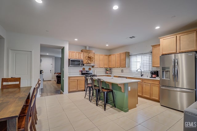 kitchen with a kitchen island, a breakfast bar, a sink, light countertops, and appliances with stainless steel finishes