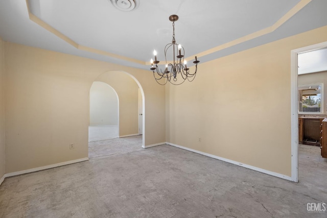 empty room featuring arched walkways, a chandelier, a raised ceiling, and concrete floors