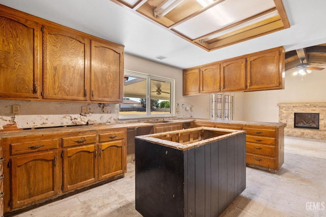 kitchen with a ceiling fan, brown cabinets, a peninsula, and a fireplace with raised hearth