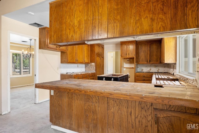 kitchen featuring brown cabinets, a chandelier, light carpet, baseboards, and a peninsula