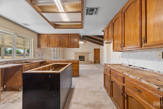 kitchen featuring decorative backsplash, brown cabinetry, a fireplace with raised hearth, and a center island