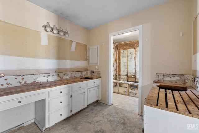 kitchen with white cabinets, unfinished concrete floors, and a sink