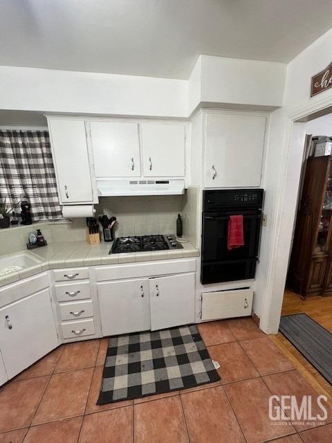 2320 Olympic Dr, Bakersfield, CA 93308 - kitchen with light tile patterned flooring, white cabinets, black appliances, and tile counters