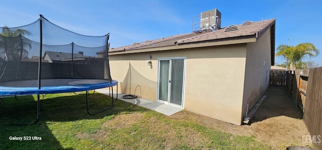 rear view of property with a trampoline, stucco siding, a yard, and central AC unit