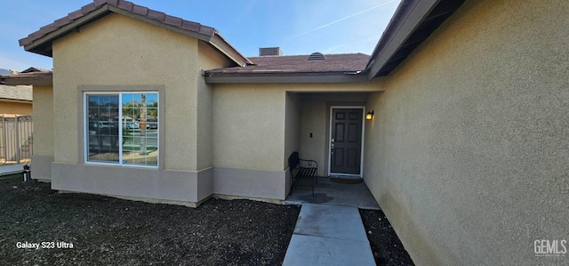 property entrance featuring a tile roof, fence, and stucco siding