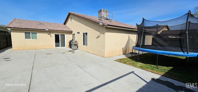 rear view of property featuring a trampoline, a patio, and stucco siding