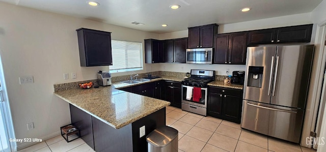 kitchen featuring light stone counters, appliances with stainless steel finishes, a sink, a peninsula, and a kitchen breakfast bar