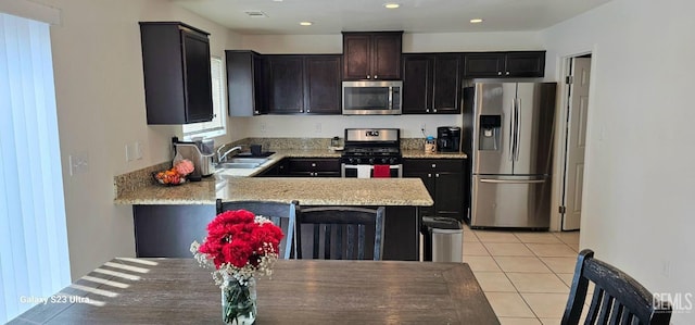 kitchen featuring appliances with stainless steel finishes, light stone counters, a peninsula, a sink, and light tile patterned flooring