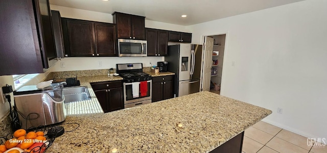 kitchen featuring stainless steel appliances, dark brown cabinets, a peninsula, and light stone countertops