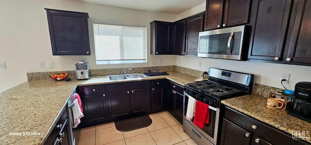 kitchen with stainless steel appliances, light stone counters, light tile patterned flooring, and a sink