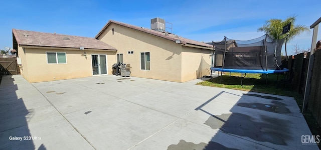 rear view of house with a trampoline, a patio, fence, and stucco siding