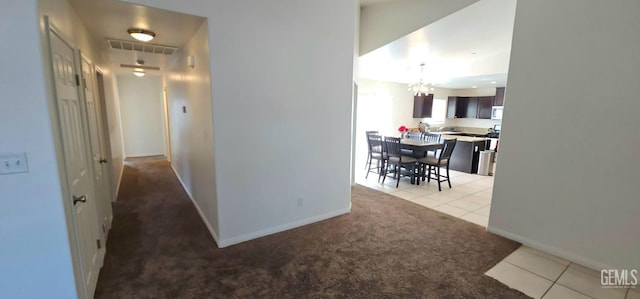 hall with baseboards, visible vents, light colored carpet, a notable chandelier, and light tile patterned flooring