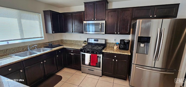 kitchen featuring light tile patterned floors, stainless steel appliances, a sink, dark brown cabinetry, and light stone countertops