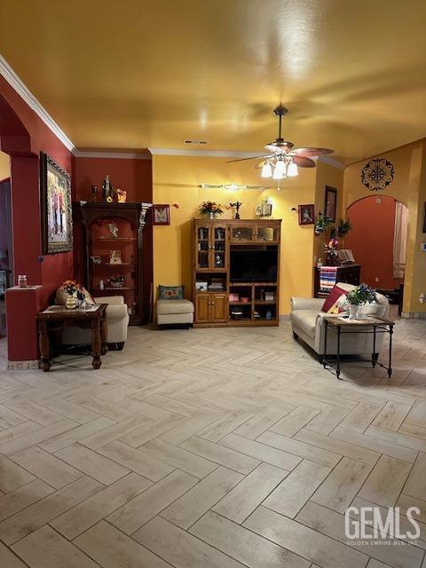 living room featuring arched walkways, a ceiling fan, and ornamental molding