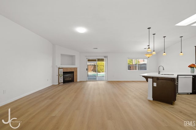 unfurnished living room with a sink, light wood-style floors, a tile fireplace, and baseboards