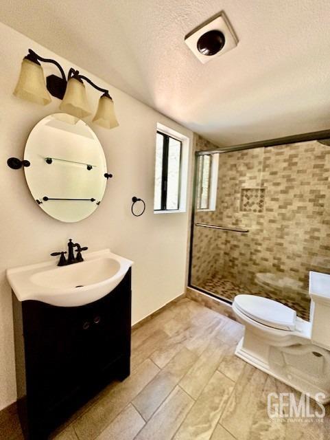 bathroom featuring a stall shower, vanity, a textured ceiling, and toilet