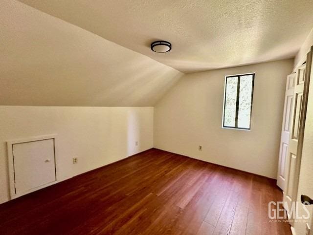 additional living space with dark wood-type flooring, a textured ceiling, and lofted ceiling
