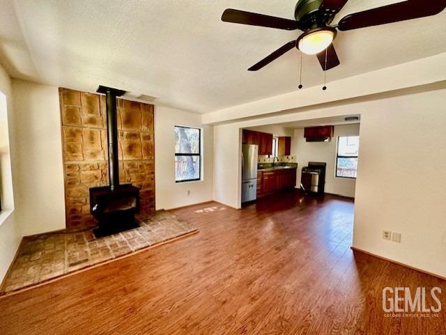 unfurnished living room with a wood stove, a wealth of natural light, baseboards, and dark wood-style floors