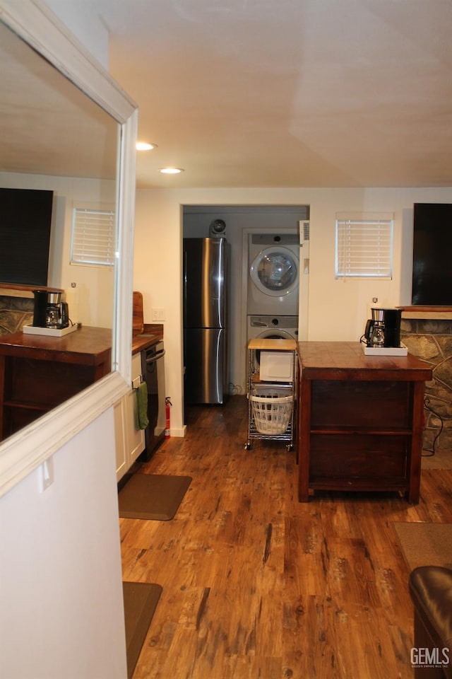 kitchen featuring stacked washer / dryer, white cabinets, black dishwasher, dark hardwood / wood-style flooring, and stainless steel refrigerator