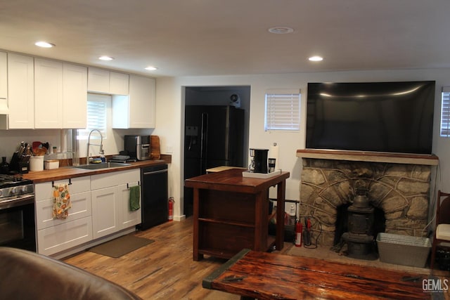 kitchen with black appliances, wooden counters, sink, and white cabinetry