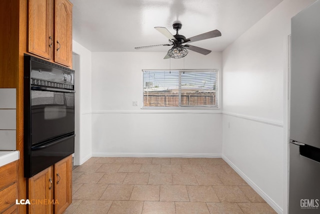 kitchen with a warming drawer, baseboards, ceiling fan, brown cabinetry, and black oven