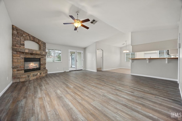 unfurnished living room featuring a large fireplace, ceiling fan with notable chandelier, wood finished floors, visible vents, and vaulted ceiling