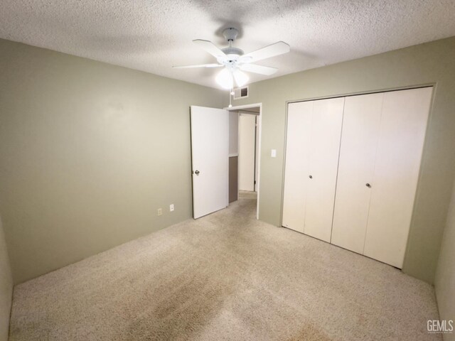 unfurnished bedroom featuring ceiling fan, light colored carpet, a textured ceiling, and a closet