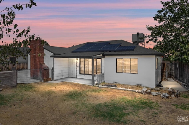 back house at dusk featuring solar panels and a yard