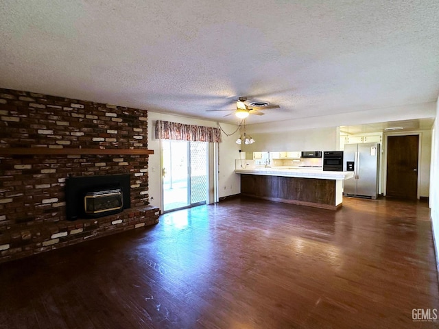 unfurnished living room with ceiling fan, a brick fireplace, dark wood-type flooring, and a textured ceiling