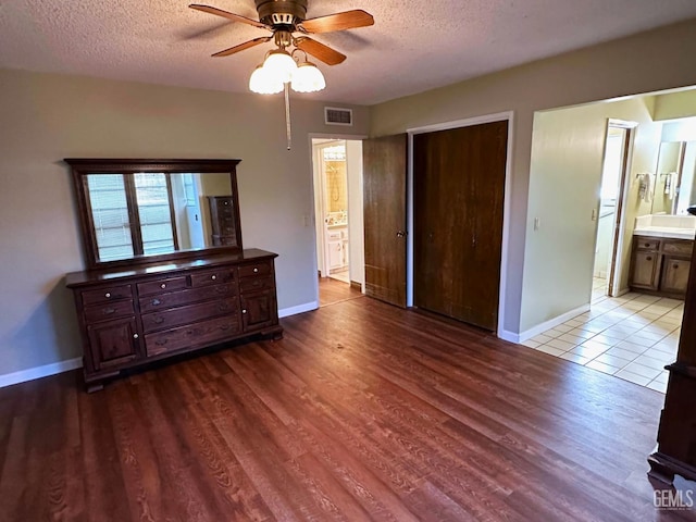 bedroom featuring light hardwood / wood-style flooring, ceiling fan, a textured ceiling, ensuite bath, and a closet