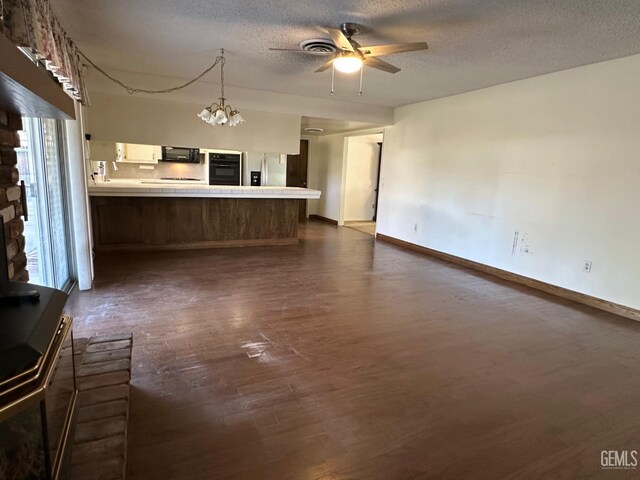 unfurnished living room featuring a textured ceiling, ceiling fan, dark hardwood / wood-style flooring, and a wood stove