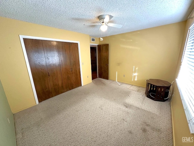 unfurnished bedroom featuring carpet flooring, a textured ceiling, a closet, ceiling fan, and multiple windows