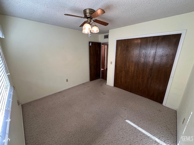 unfurnished bedroom featuring a textured ceiling, a closet, light colored carpet, and ceiling fan