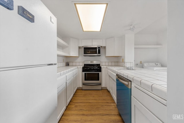 kitchen featuring ceiling fan, appliances with stainless steel finishes, tile counters, white cabinetry, and washer / clothes dryer