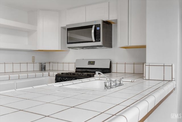 kitchen featuring white cabinets, tile counters, black gas stove, and sink