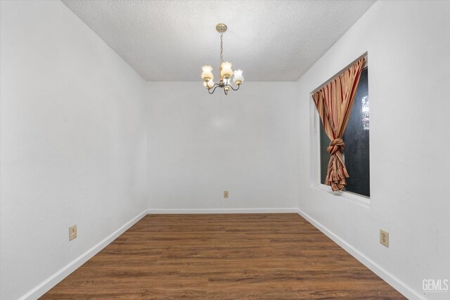 spare room featuring a textured ceiling, dark hardwood / wood-style floors, and an inviting chandelier