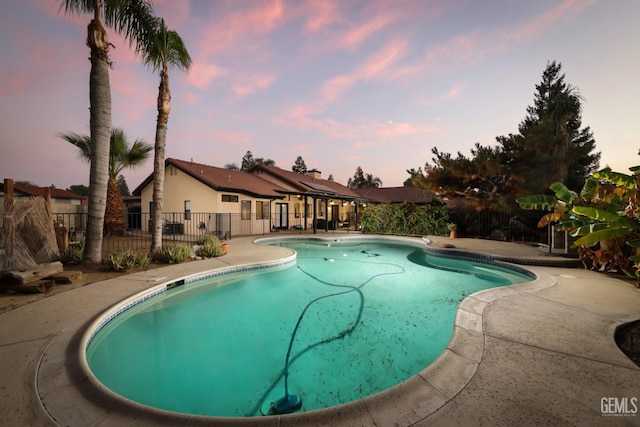 pool at dusk with a patio, fence, and a fenced in pool