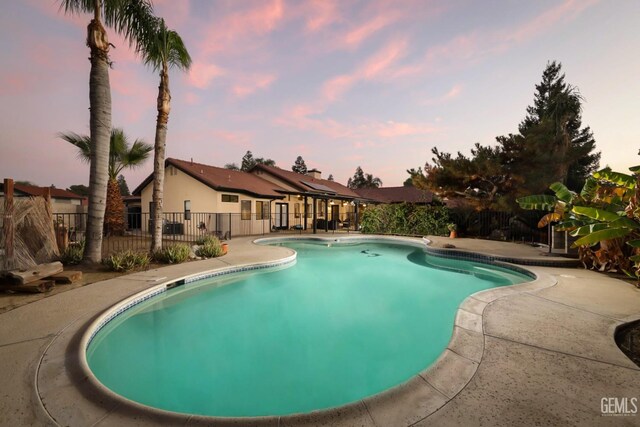 pool at dusk with a patio, fence, and a fenced in pool