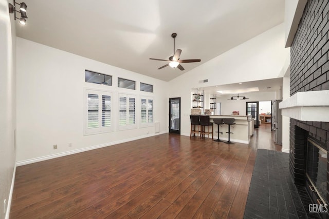 unfurnished living room featuring high vaulted ceiling, a ceiling fan, baseboards, a brick fireplace, and dark wood finished floors