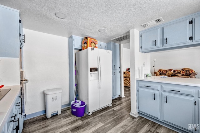 kitchen with a textured ceiling, dark wood-type flooring, visible vents, light countertops, and white fridge with ice dispenser