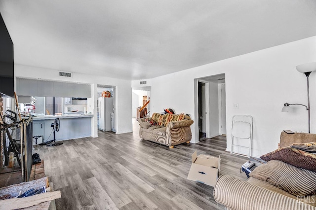 living room featuring light wood-style flooring, visible vents, and stairway