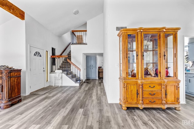 entrance foyer with stairway, light wood-style flooring, visible vents, and high vaulted ceiling