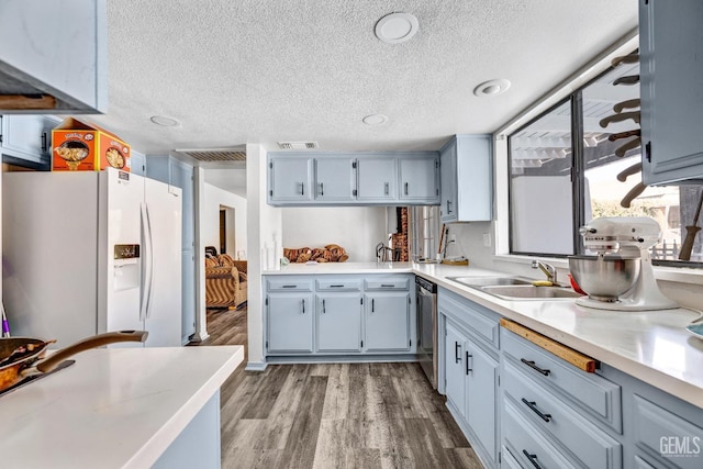 kitchen with dishwasher, wood finished floors, light countertops, white fridge with ice dispenser, and a sink