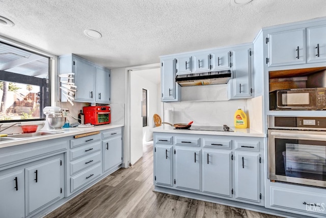 kitchen featuring light wood finished floors, black microwave, light countertops, under cabinet range hood, and stainless steel oven